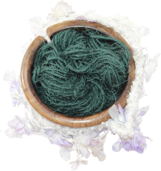 Dark green KnitSilk Artisan linen yarn arranged in a wooden bowl surrounded by pale flowers
